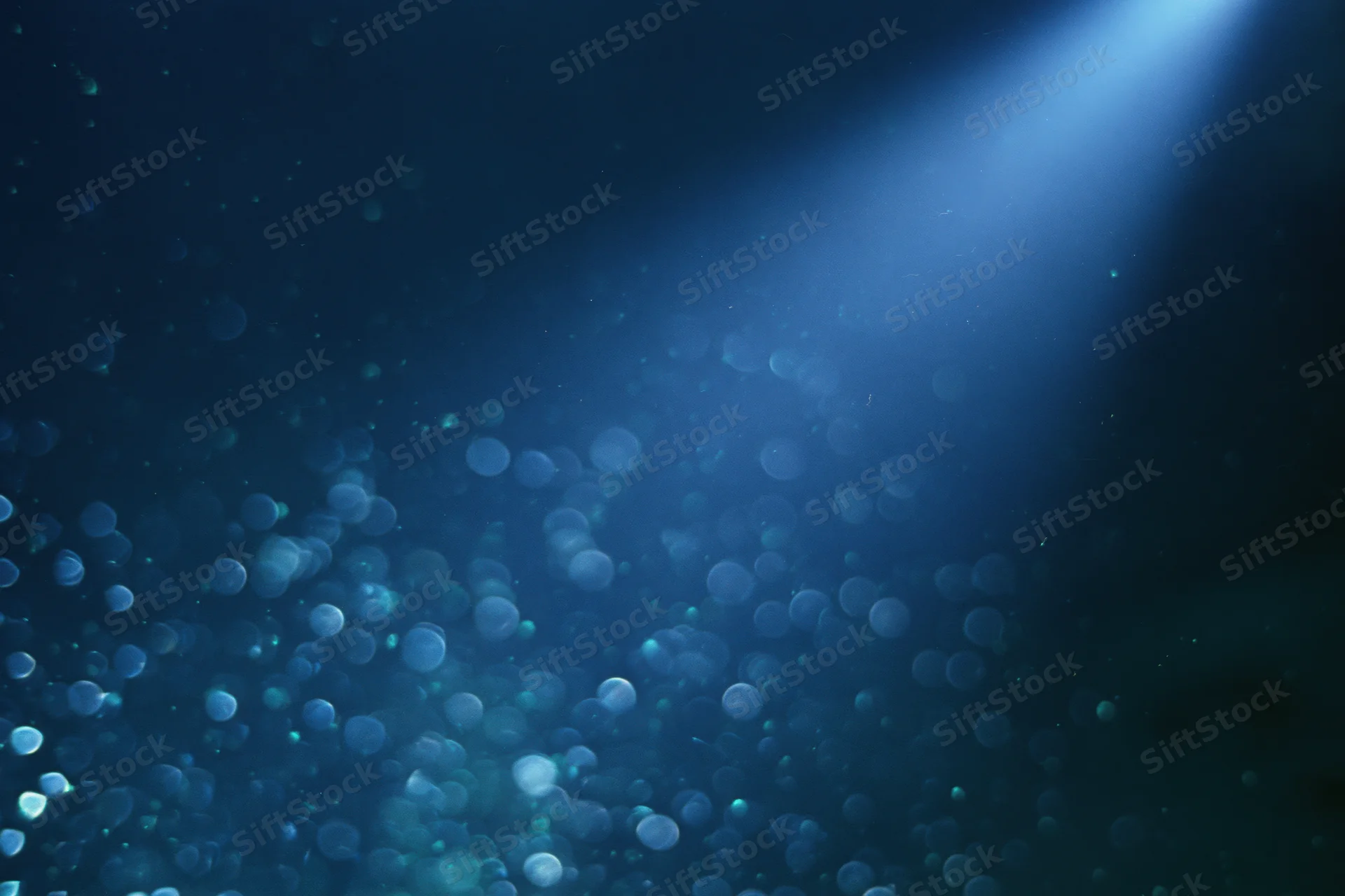 Abstract dark blue background with floating out-of-focus light particles and a glowing beam from above