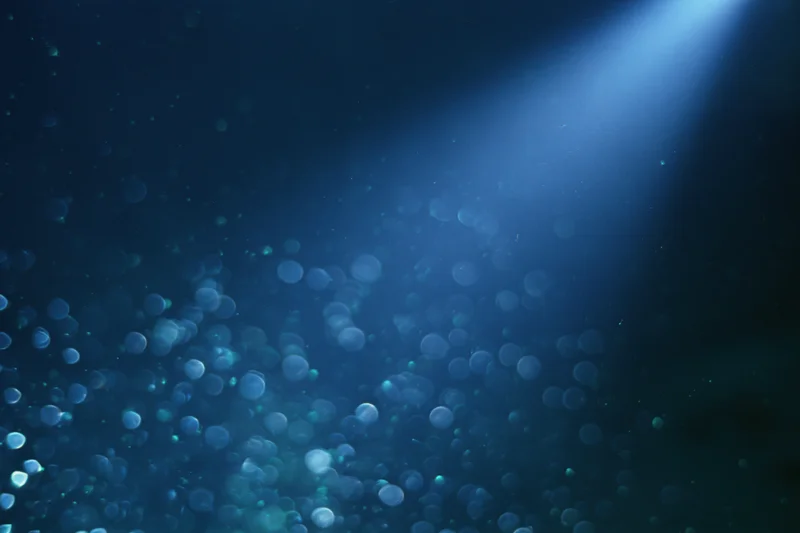 Abstract dark blue background with floating out-of-focus light particles and a glowing beam from above