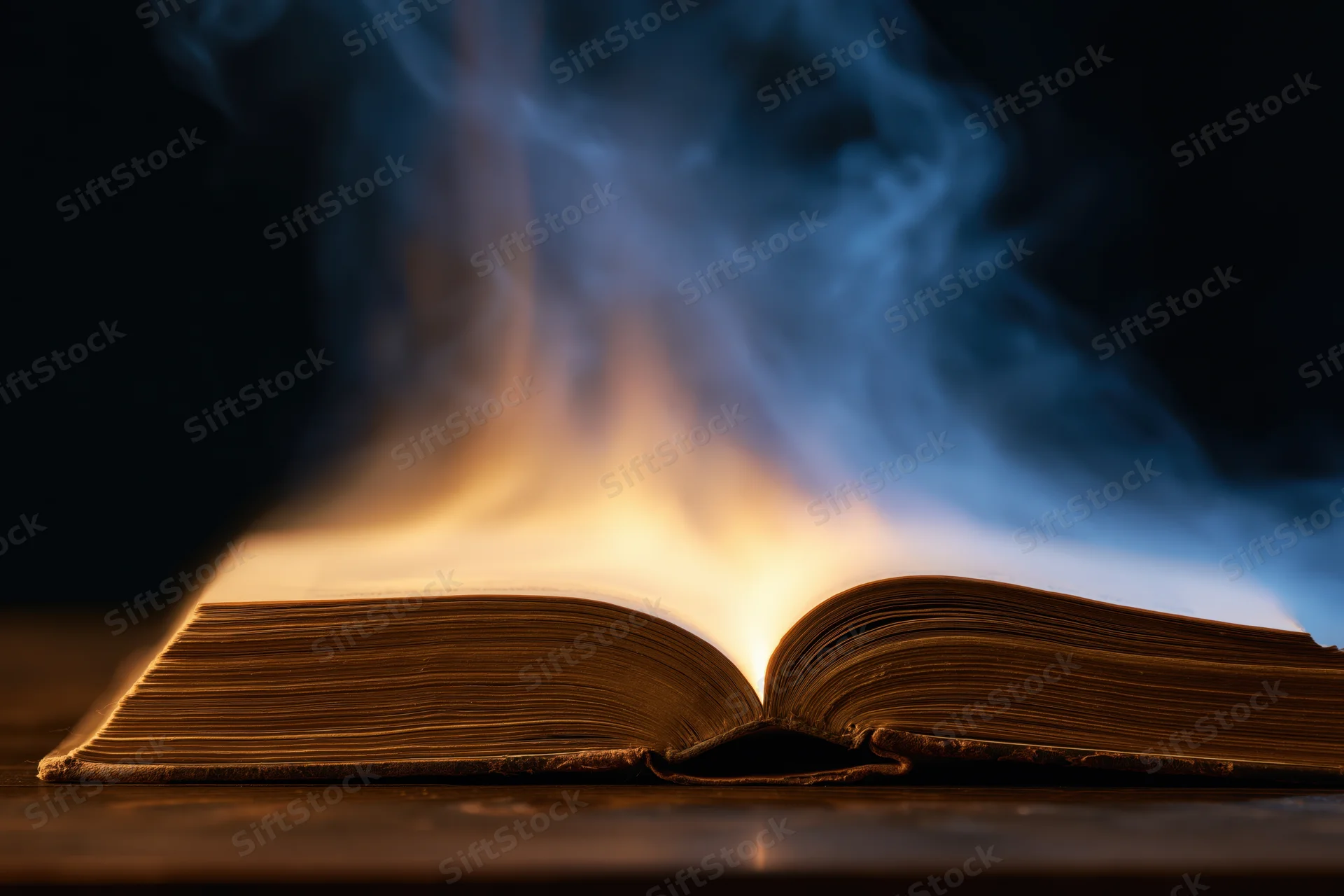 Open antique book burning with blue and orange flames on dark wooden surface