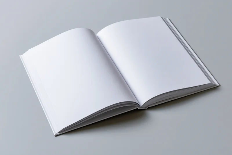 Open hardcover book lying flat with blank white pages on gray surface