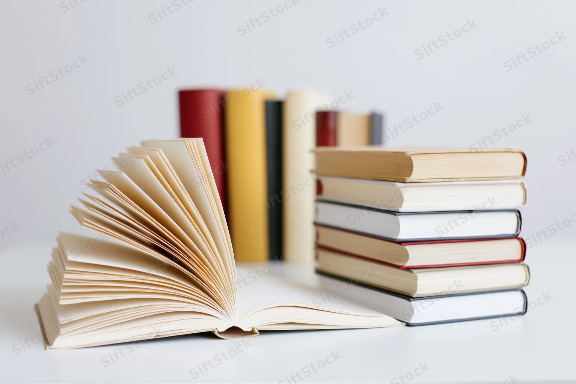 Open hardcover book with fanned pages beside a stack of books on white surface