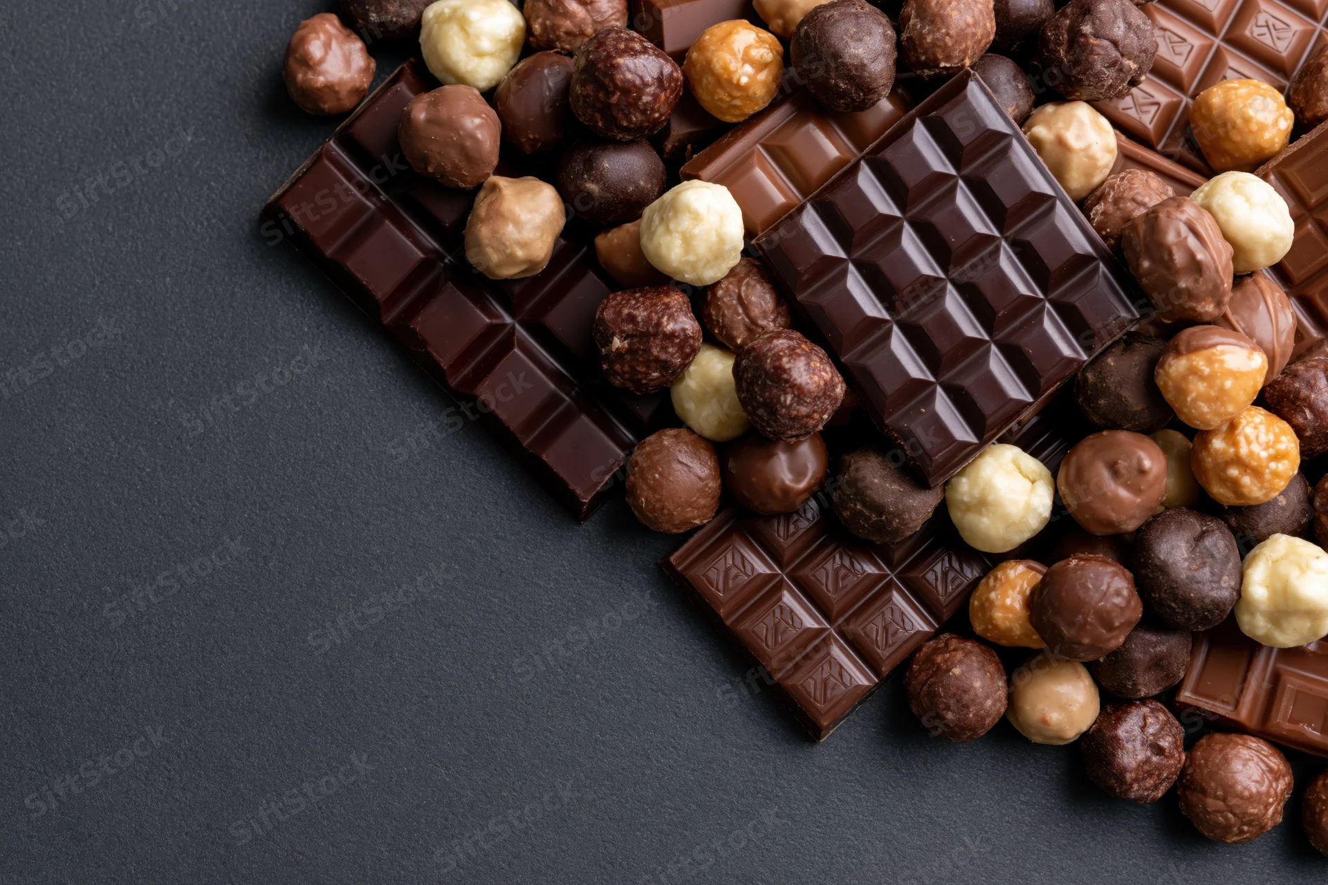 Assorted chocolate bars and pralines arranged in a loose pile on a dark surface