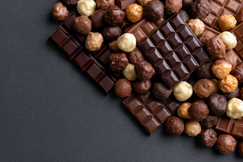 Assorted chocolate bars and pralines arranged in a loose pile on a dark surface