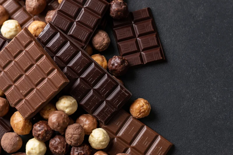 Assorted chocolate bars and pralines arranged in a loose pile on a dark surface with copyspace