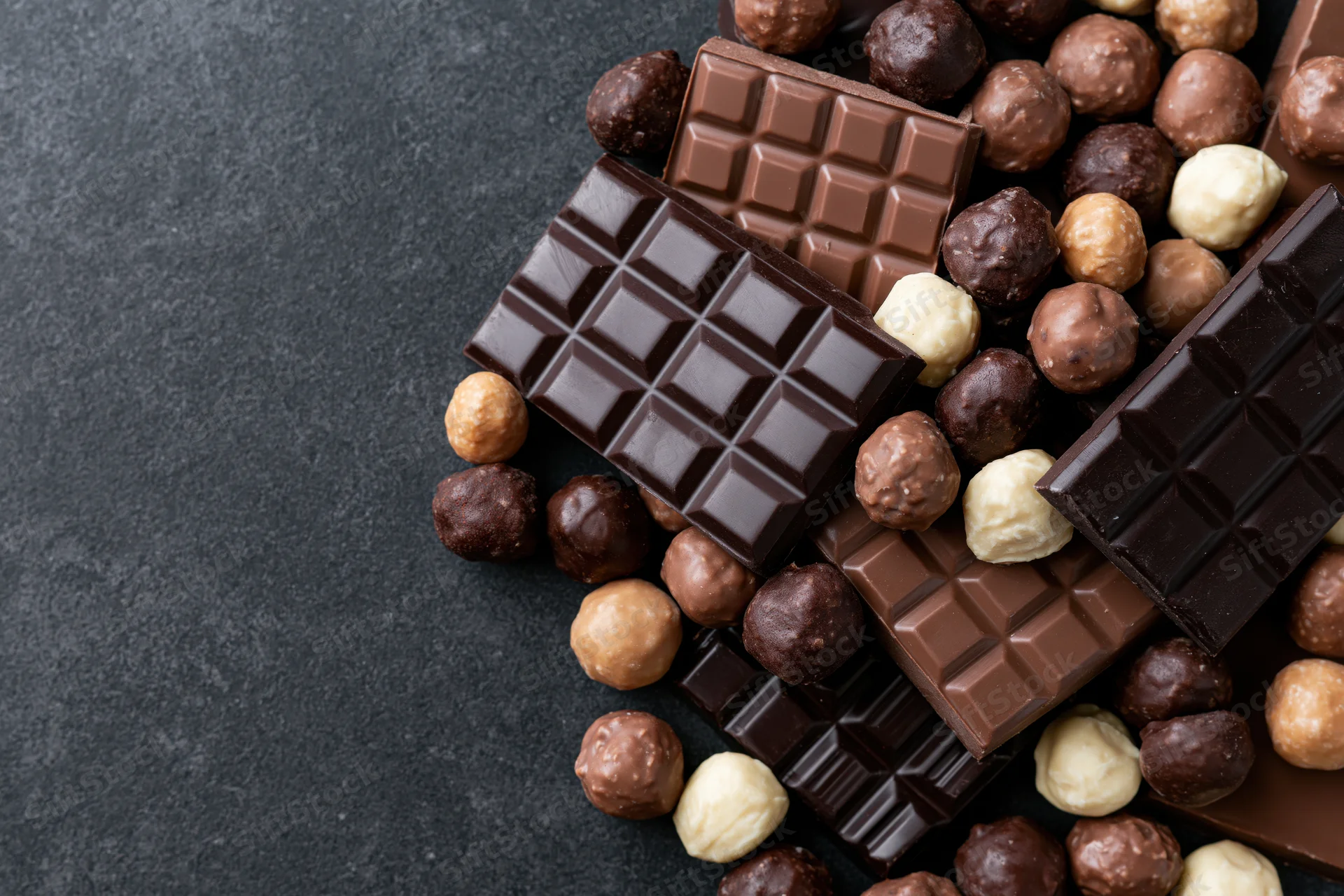 Assorted chocolate bars and pralines arranged in a loose pile on dark surface