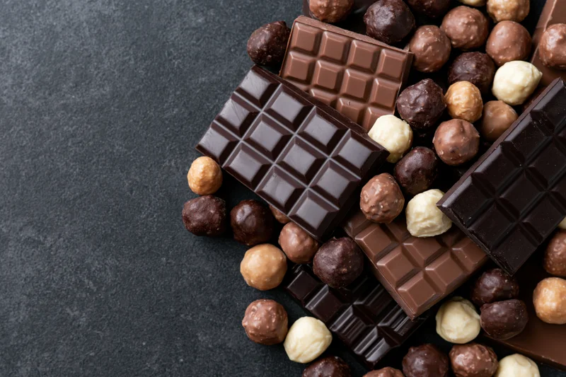 Assorted chocolate bars and pralines arranged in a loose pile on dark surface