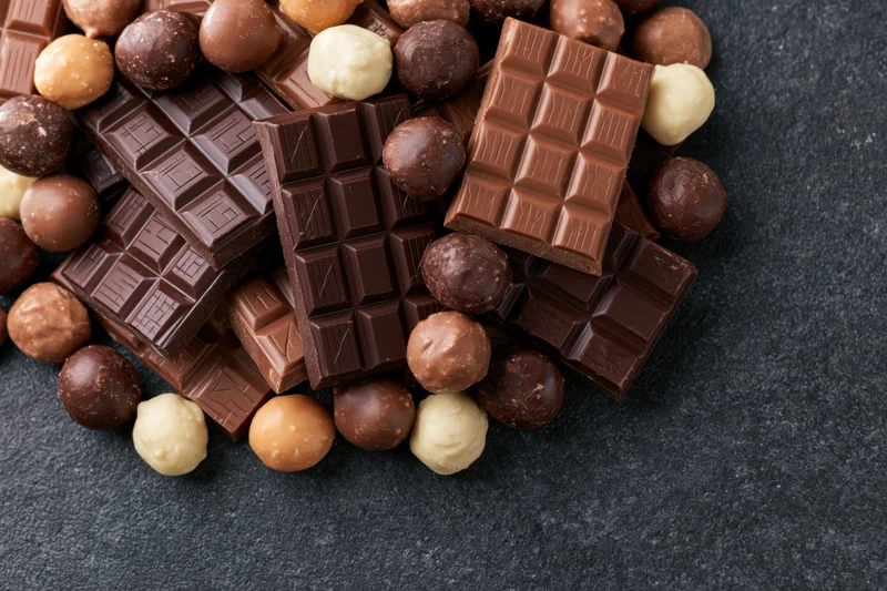 Assorted chocolate bars and pralines piled on a dark slate surface