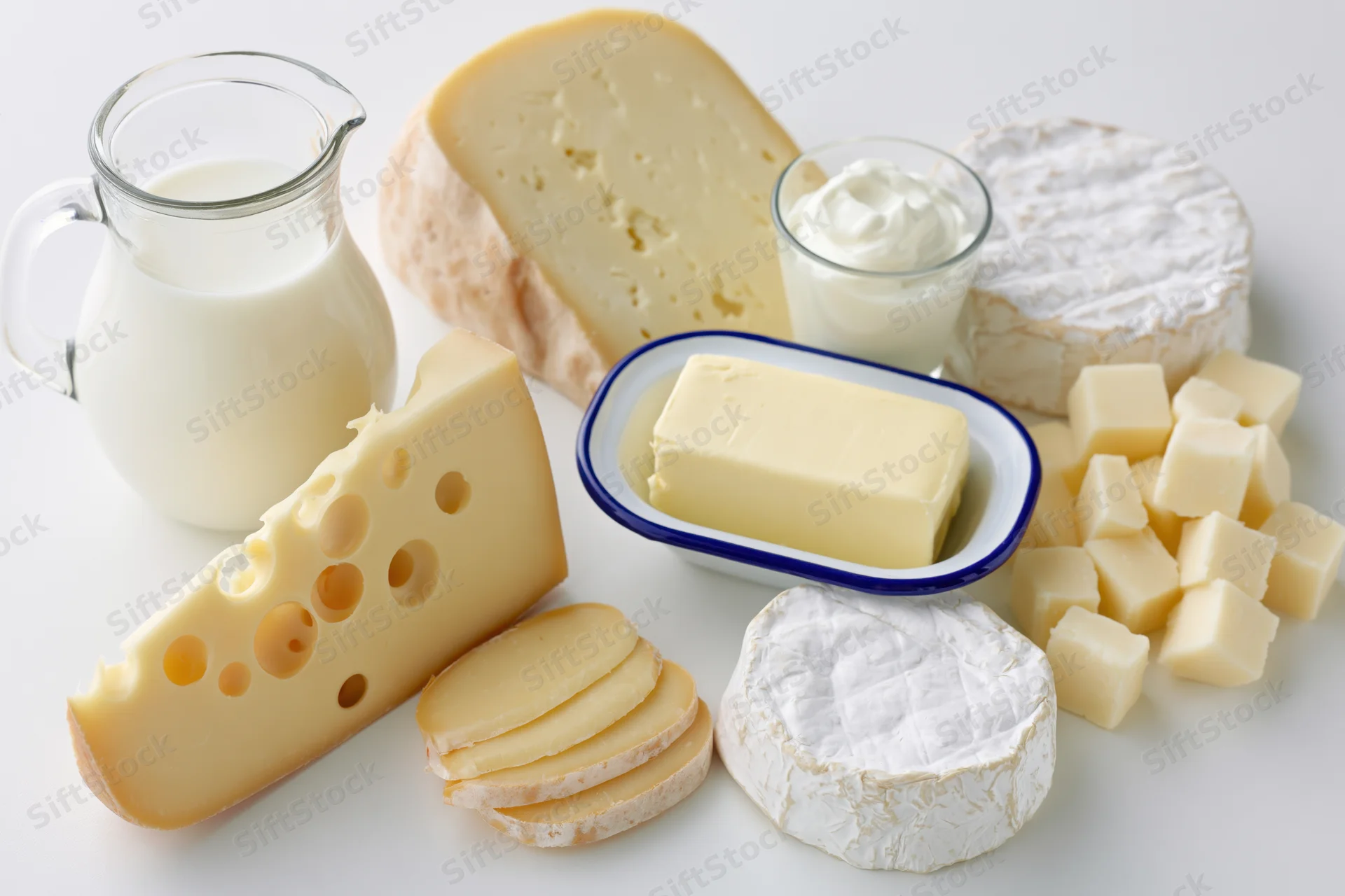 Assorted dairy products arranged on a white surface including cheese, milk, butter and yogurt