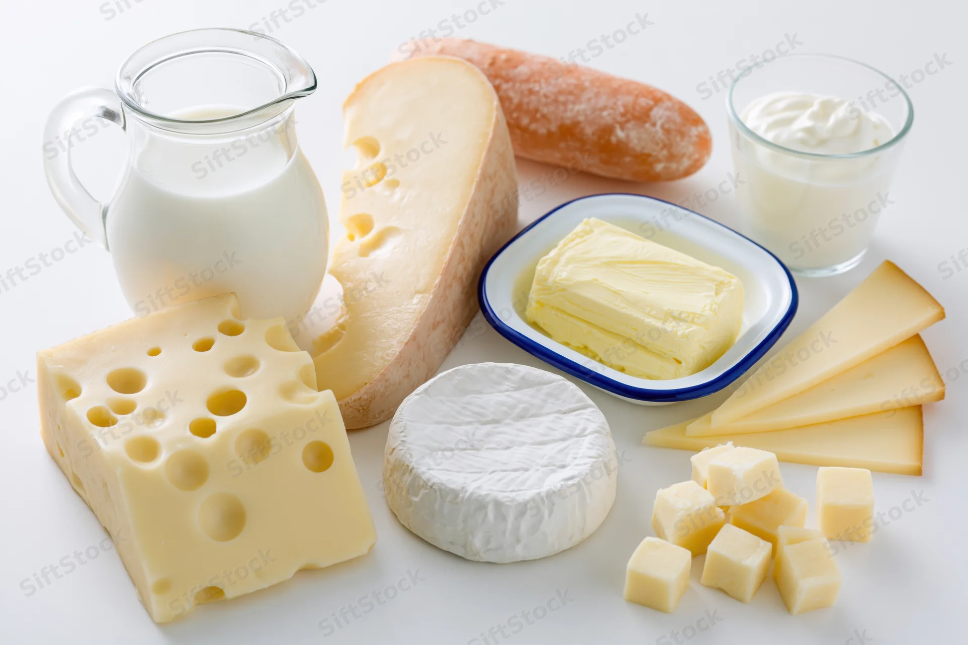 Assorted dairy products arranged on a white surface including cheese, milk, butter, and yogurt
