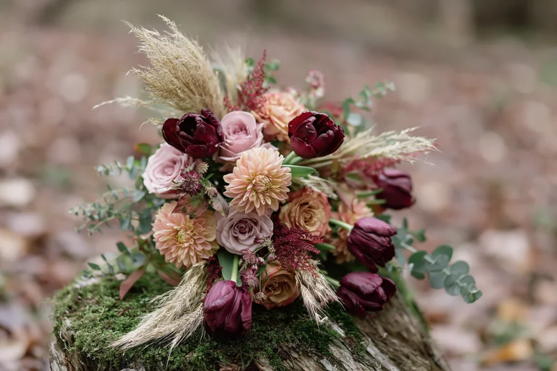 Autumn wedding bouquet with roses, tulips and pampas grass resting on a moss-covered wooden stump