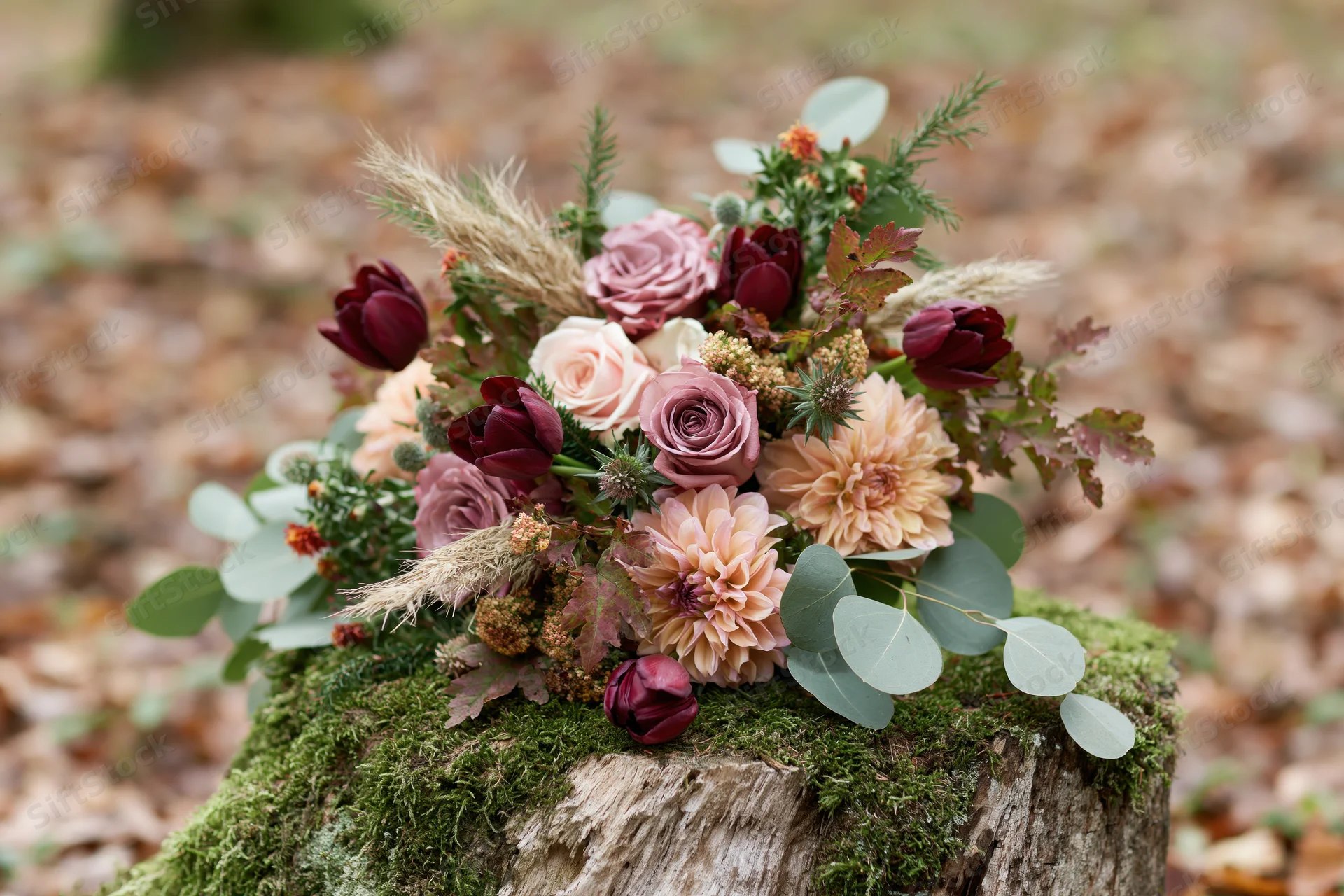 Autumn wedding bouquet arranged with roses, dahlias, and greenery resting on a moss-covered wooden stump in a forest setting