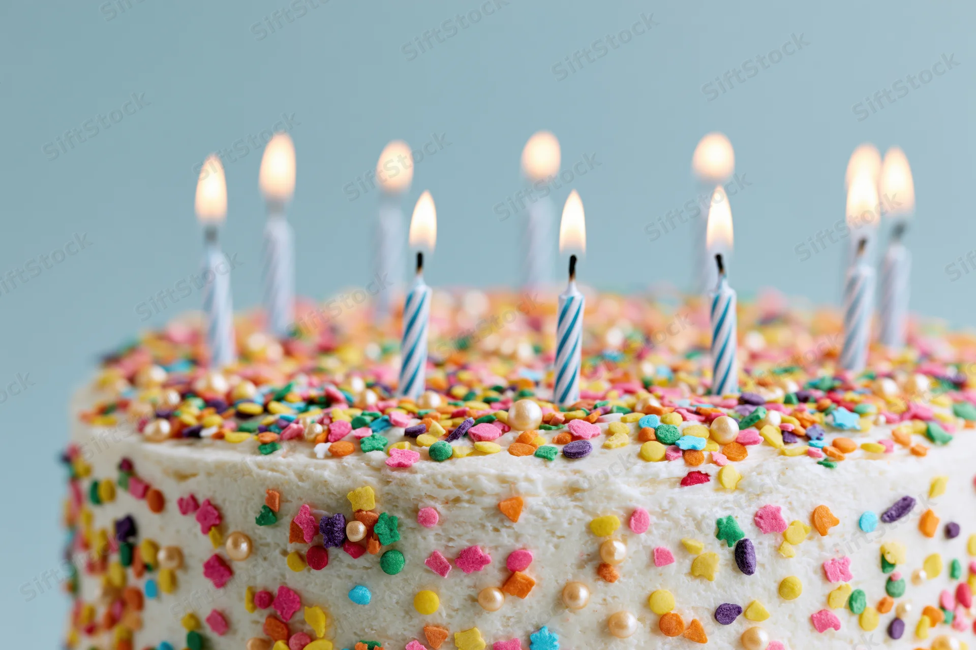 Birthday cake with white frosting and multicolored sprinkles topped with lit candles, close-up view