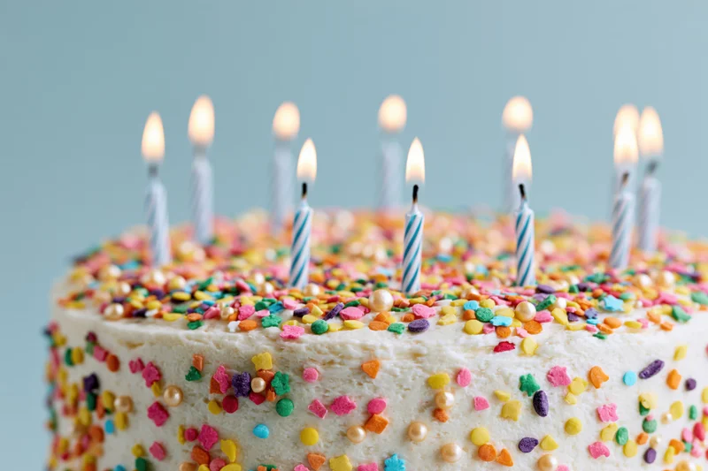 Birthday cake with white frosting and multicolored sprinkles topped with lit candles, close-up view