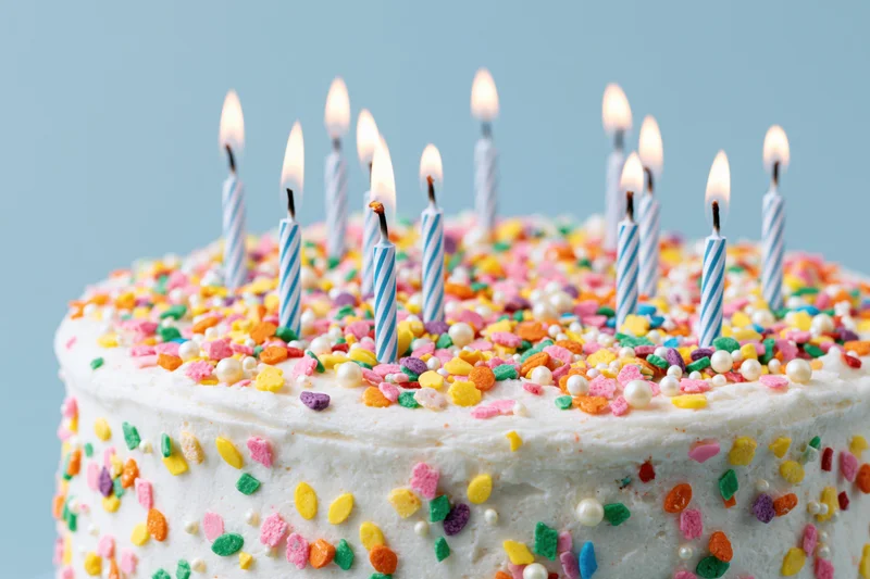 Birthday cake with white frosting and colorful sprinkles topped with lit striped candles