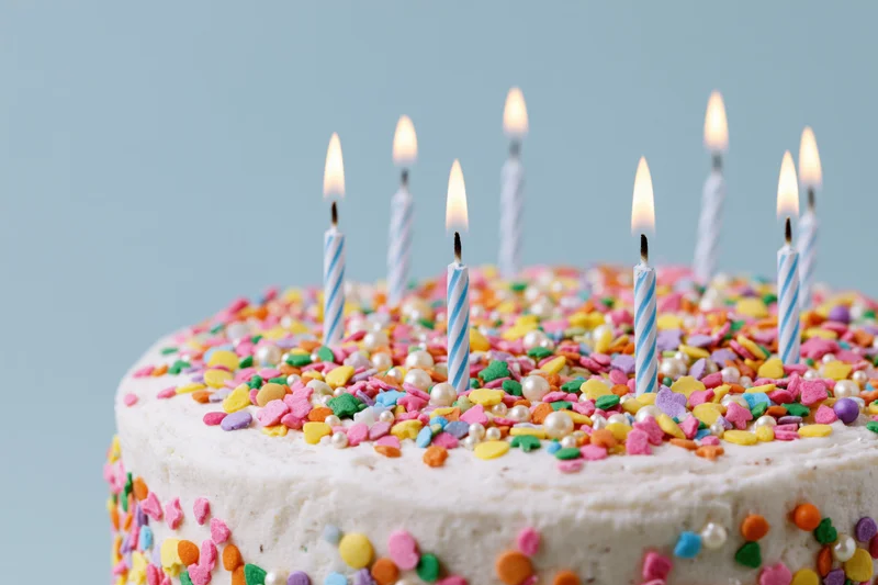 Birthday cake with white frosting and colorful sprinkles topped with lit candles