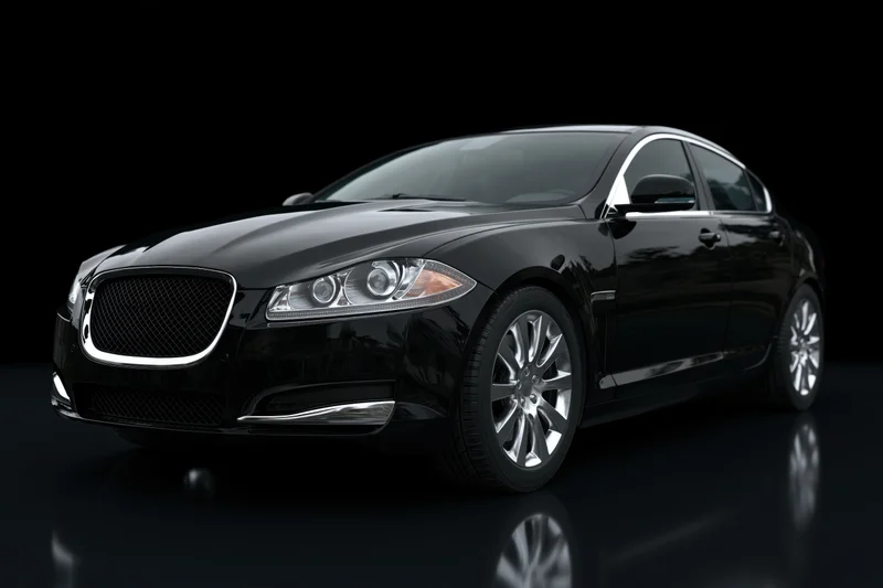 Black luxury sedan viewed from low front threequarter angle in dark studio with reflections on glossy floor
