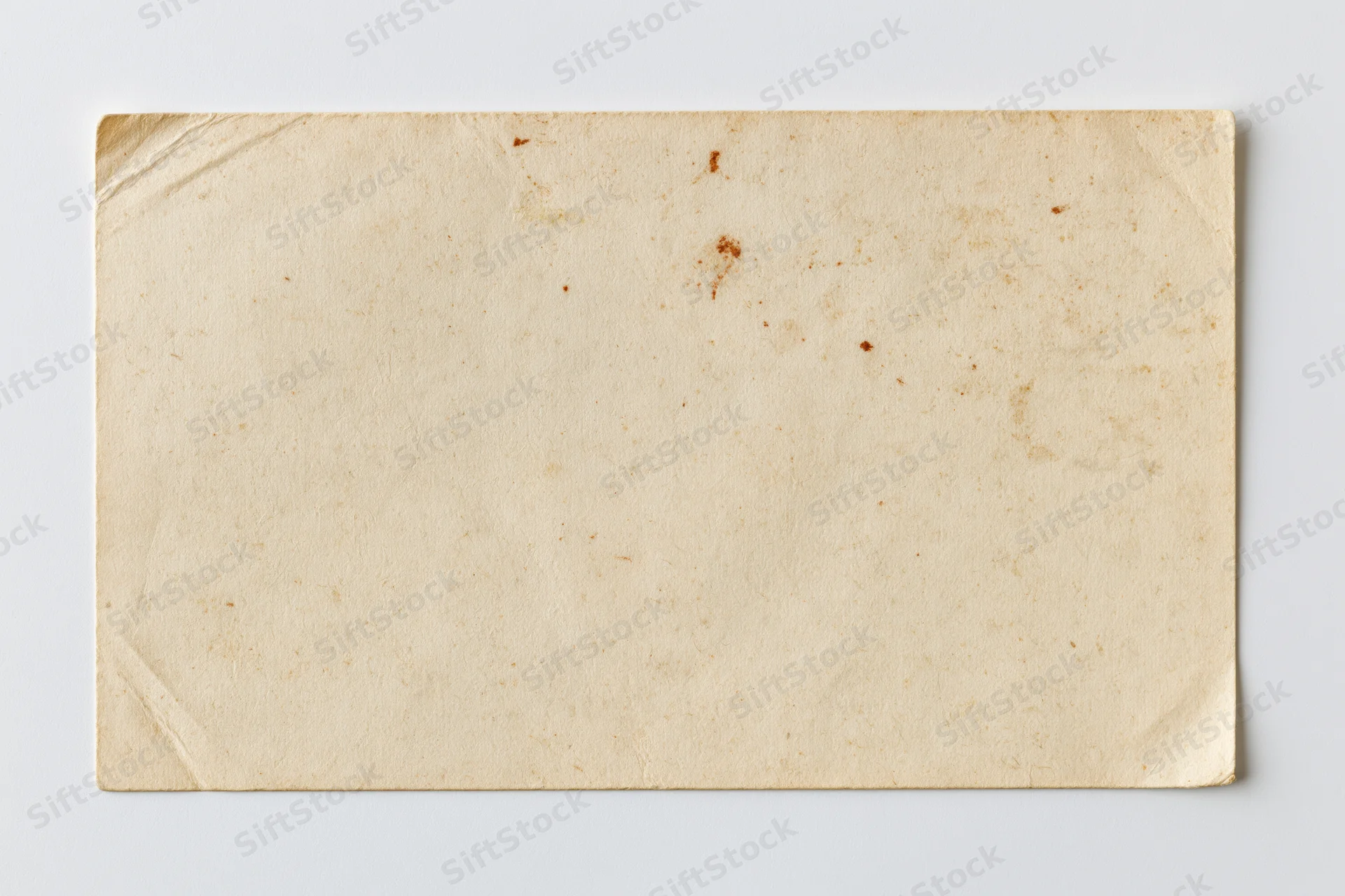 Blank vintage postcard lying flat on white surface with visible creases and stains