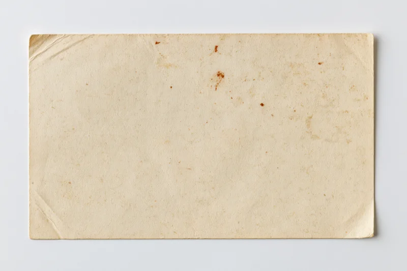 Blank vintage postcard lying flat on white surface with visible creases and stains