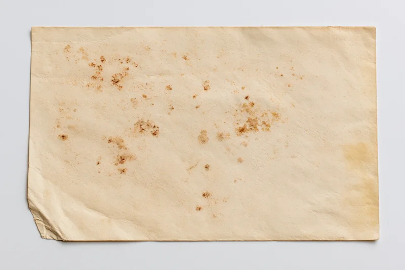 Blank vintage postcard lying flat on white surface with stains and creases