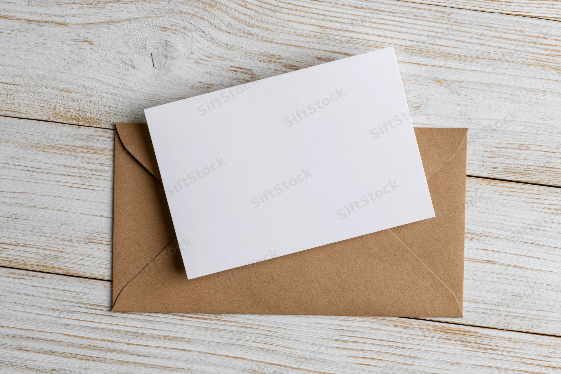 Blank white card resting on a kraft paper envelope on a wooden surface