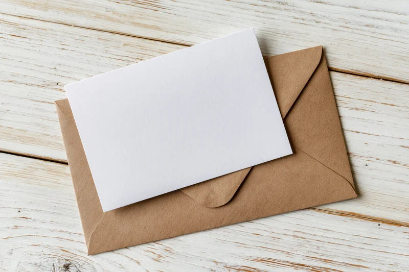 Blank white card resting on kraft envelope on wooden surface