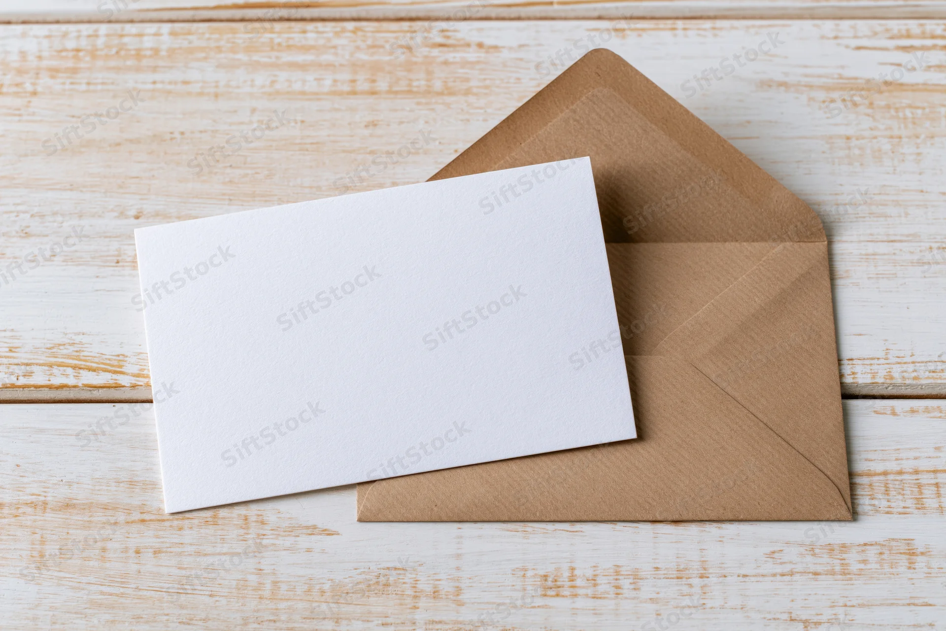 Blank white card resting on a kraft paper envelope on a wooden surface