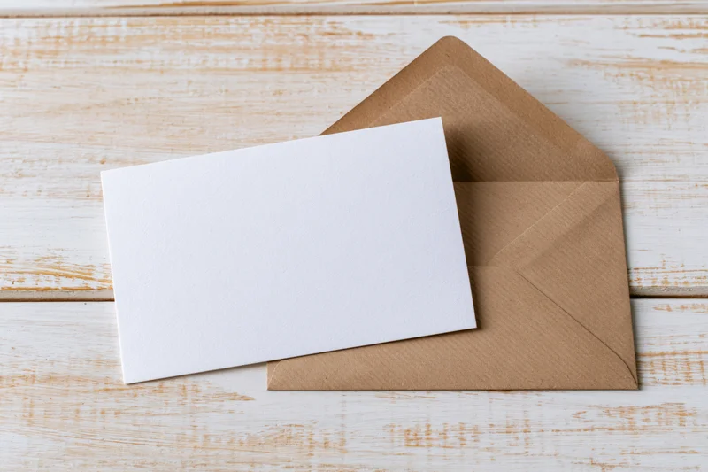 Blank white card resting on a kraft paper envelope on a wooden surface