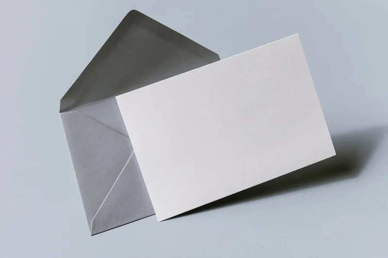 Blank white card leaning against open grey envelope on plain surface