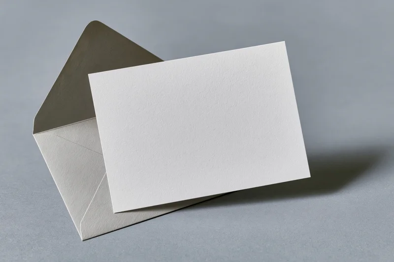 Blank white card leaning against open grey envelope on flat surface