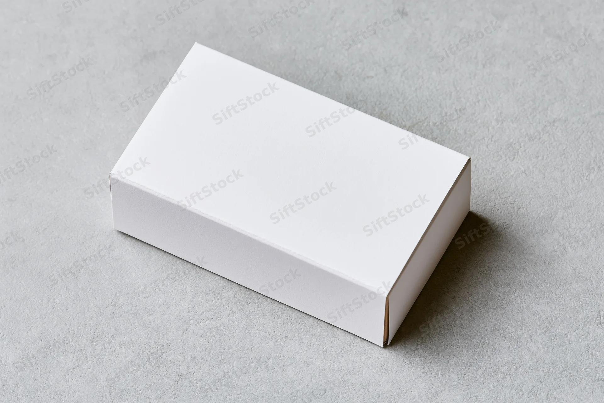 White rectangular cardboard box lying flat on a gray concrete surface with lid closed and shadow cast to the right