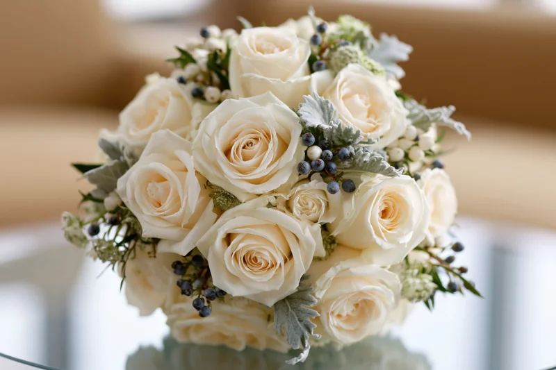 Bridal bouquet of cream and white roses arranged in a rounded shape with greenery and berries