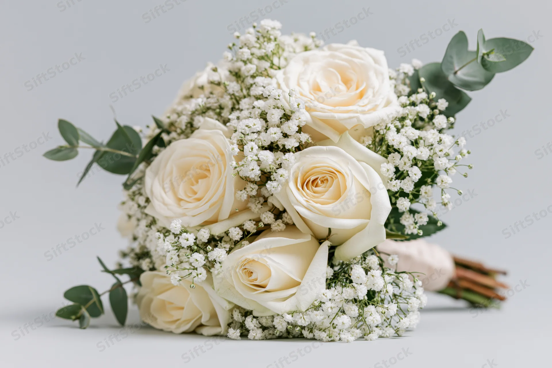 Bridal bouquet of cream white roses, baby's breath, and eucalyptus arranged on a plain surface