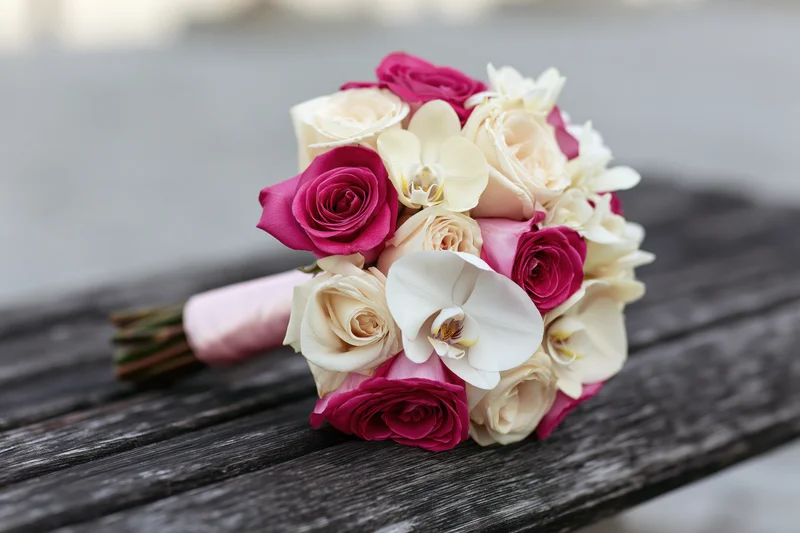 Bridal bouquet of pink roses and cream orchids resting on wooden table