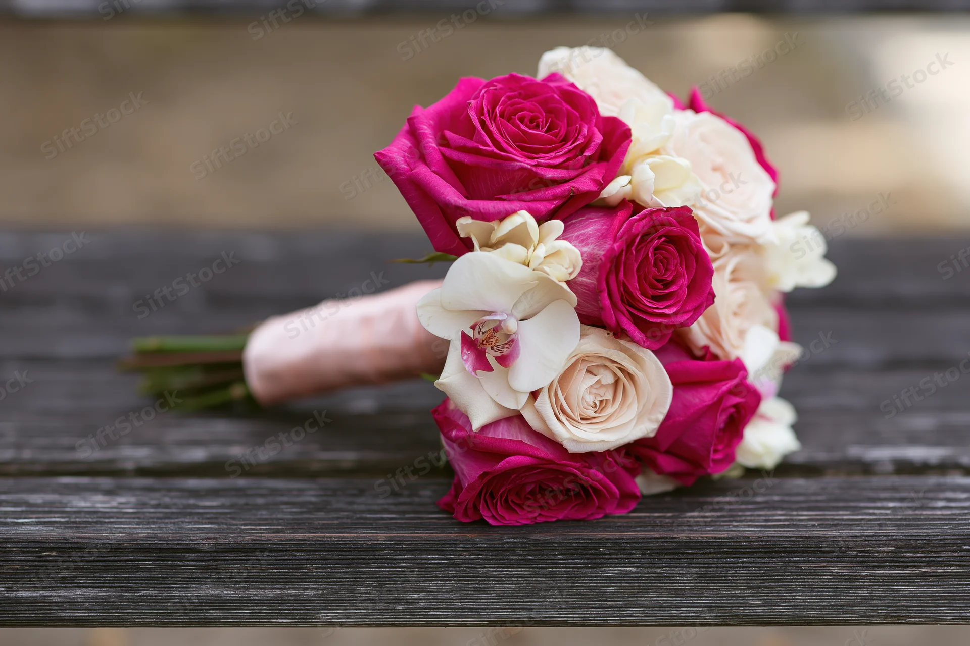 Bridal bouquet of pink roses and cream orchids resting on wooden bench