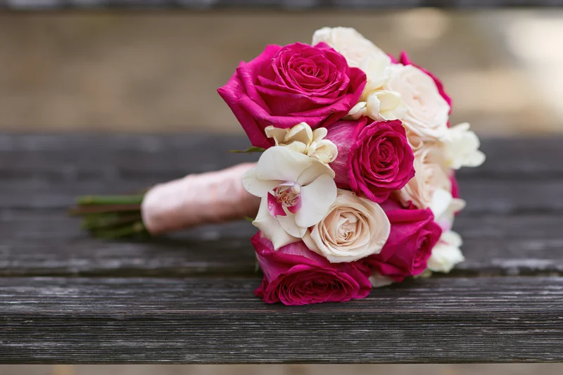 Bridal bouquet of pink roses and cream orchids resting on wooden bench