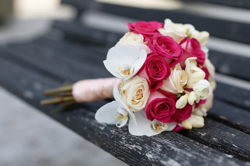 Bridal bouquet of pink roses and cream orchids resting on a weathered wooden bench