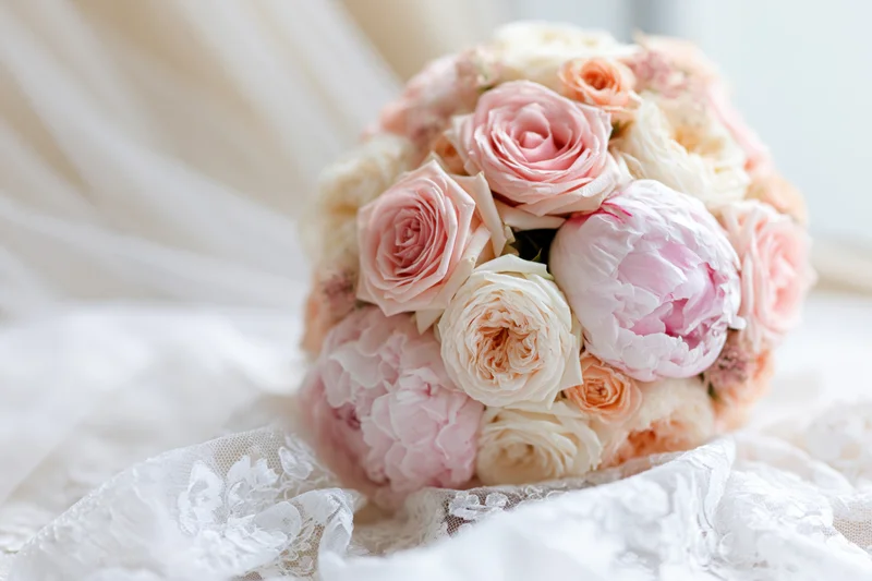 Bridal bouquet of pink roses and peonies resting on white lace fabric