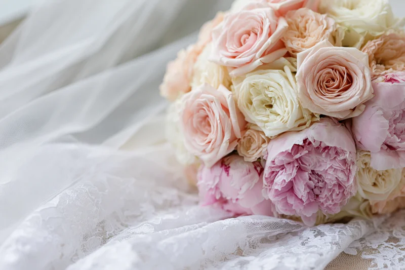 Bridal bouquet of pink roses and peonies resting on white lace fabric