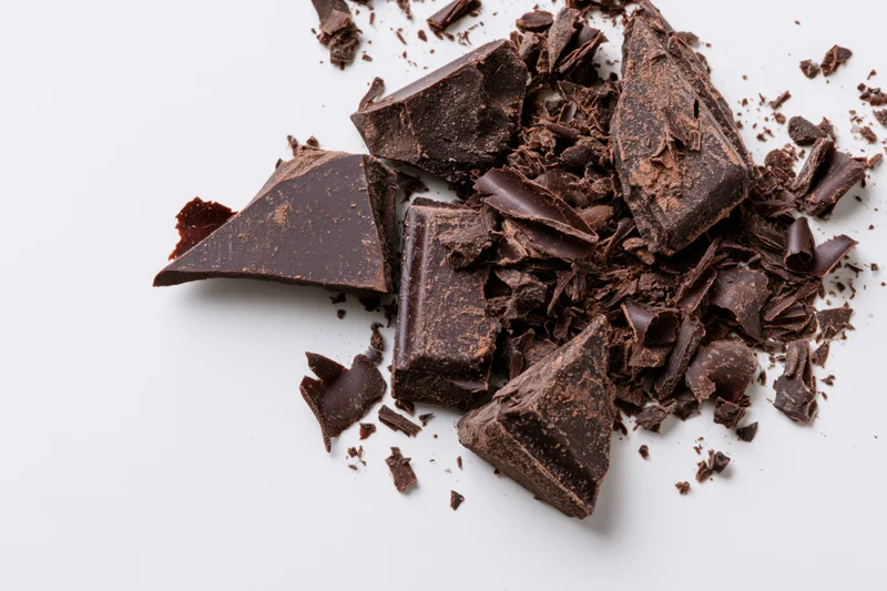 Broken dark chocolate chunks and shavings scattered across a white background