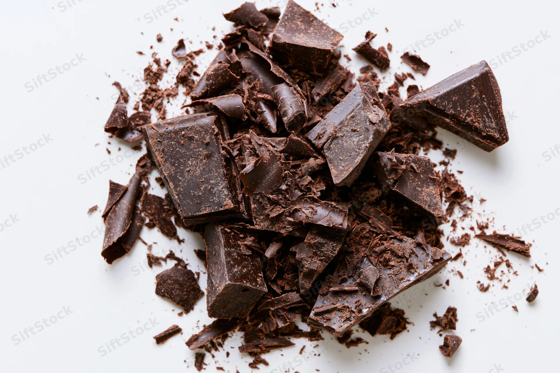 Broken dark chocolate chunks and shavings scattered across a white surface