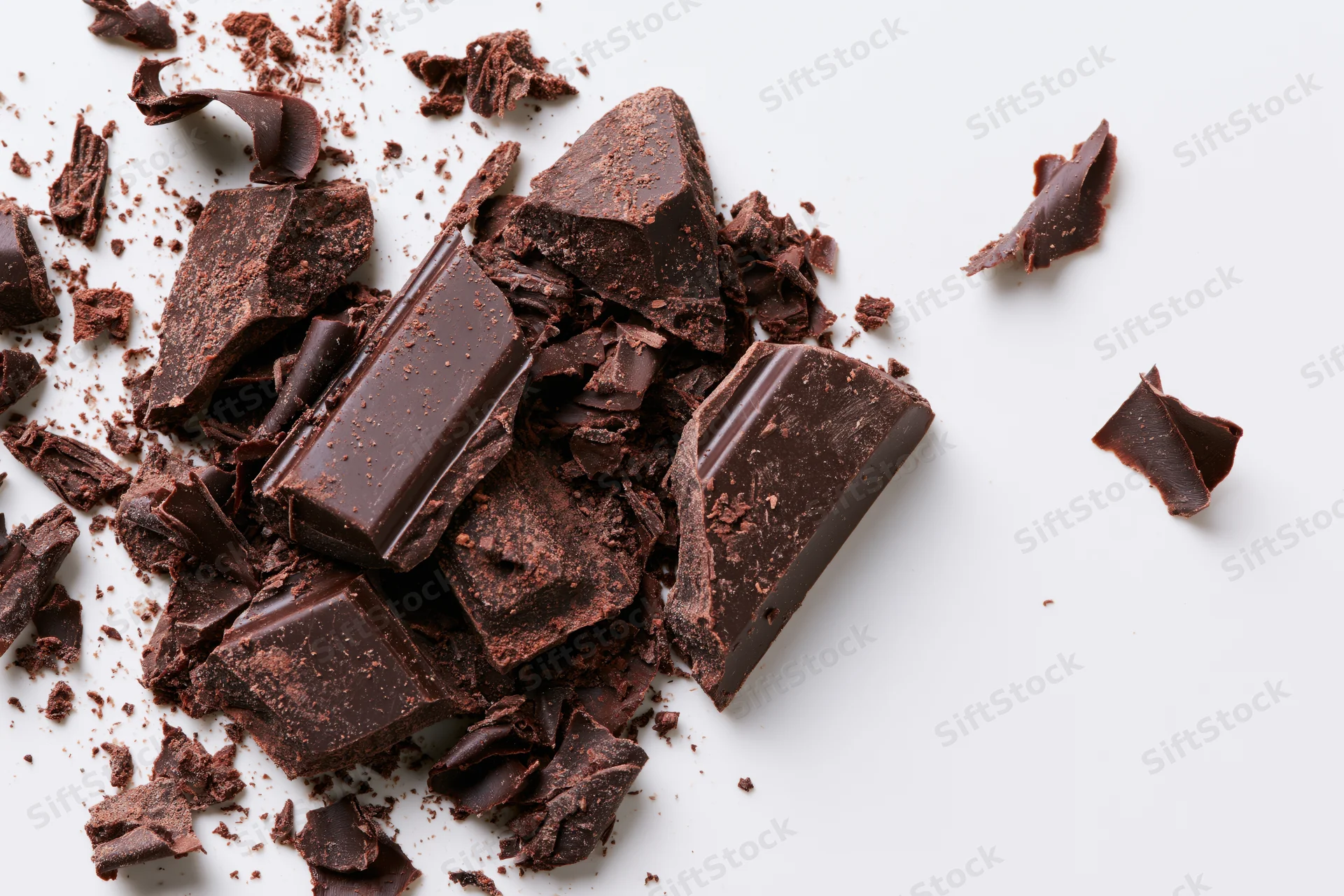 Broken dark chocolate chunks and shavings scattered across a white surface