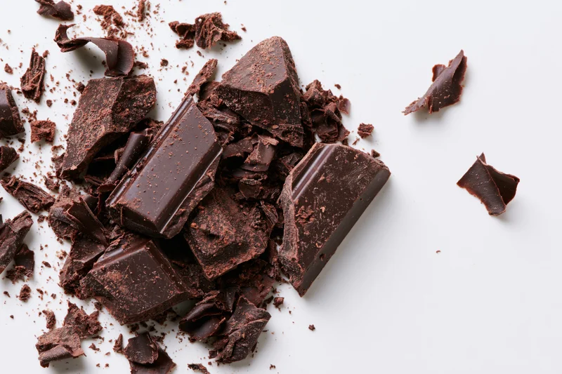 Broken dark chocolate chunks and shavings scattered across a white surface