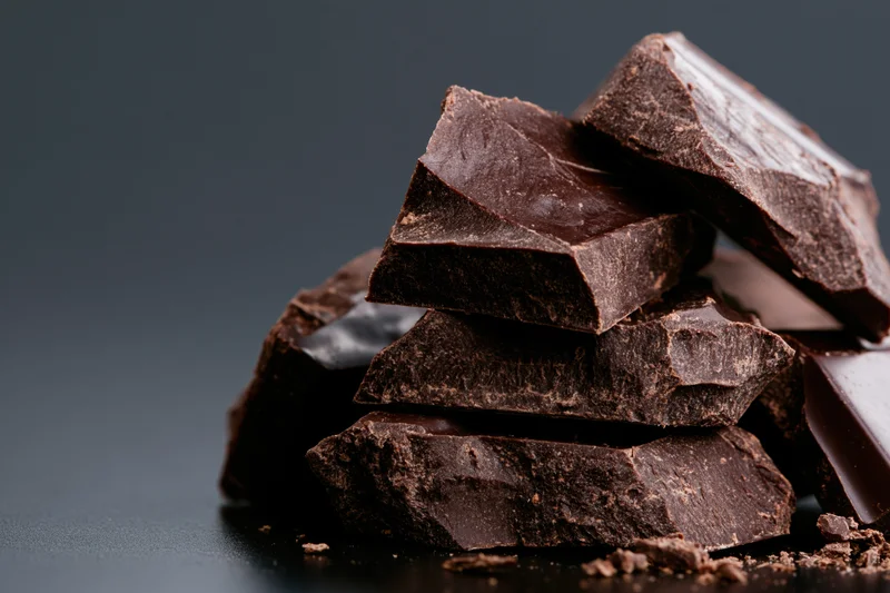 Broken dark chocolate chunks stacked into a rough tower on a dark surface with copyspace