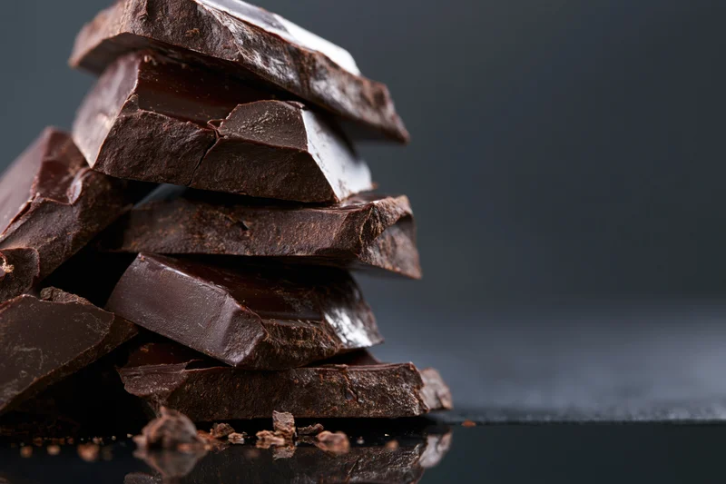 Broken dark chocolate chunks stacked into a rough tower on a reflective black surface
