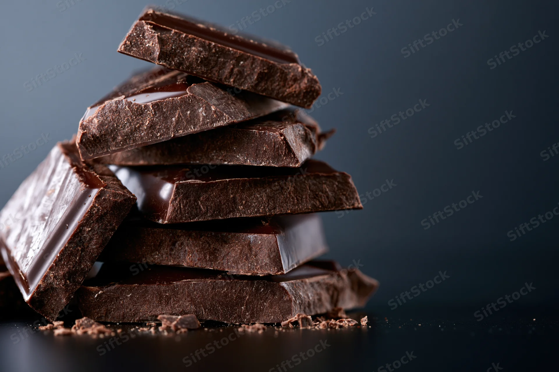 Broken dark chocolate chunks stacked into a rough tower on a dark surface with copyspace