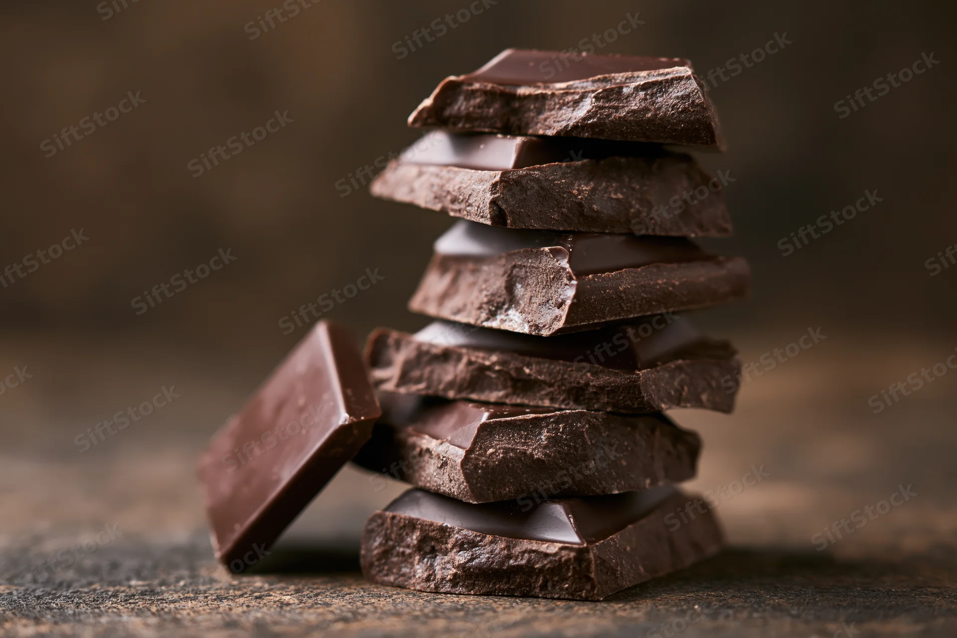 Broken dark chocolate pieces stacked unevenly into a tall tower on a rustic stone surface