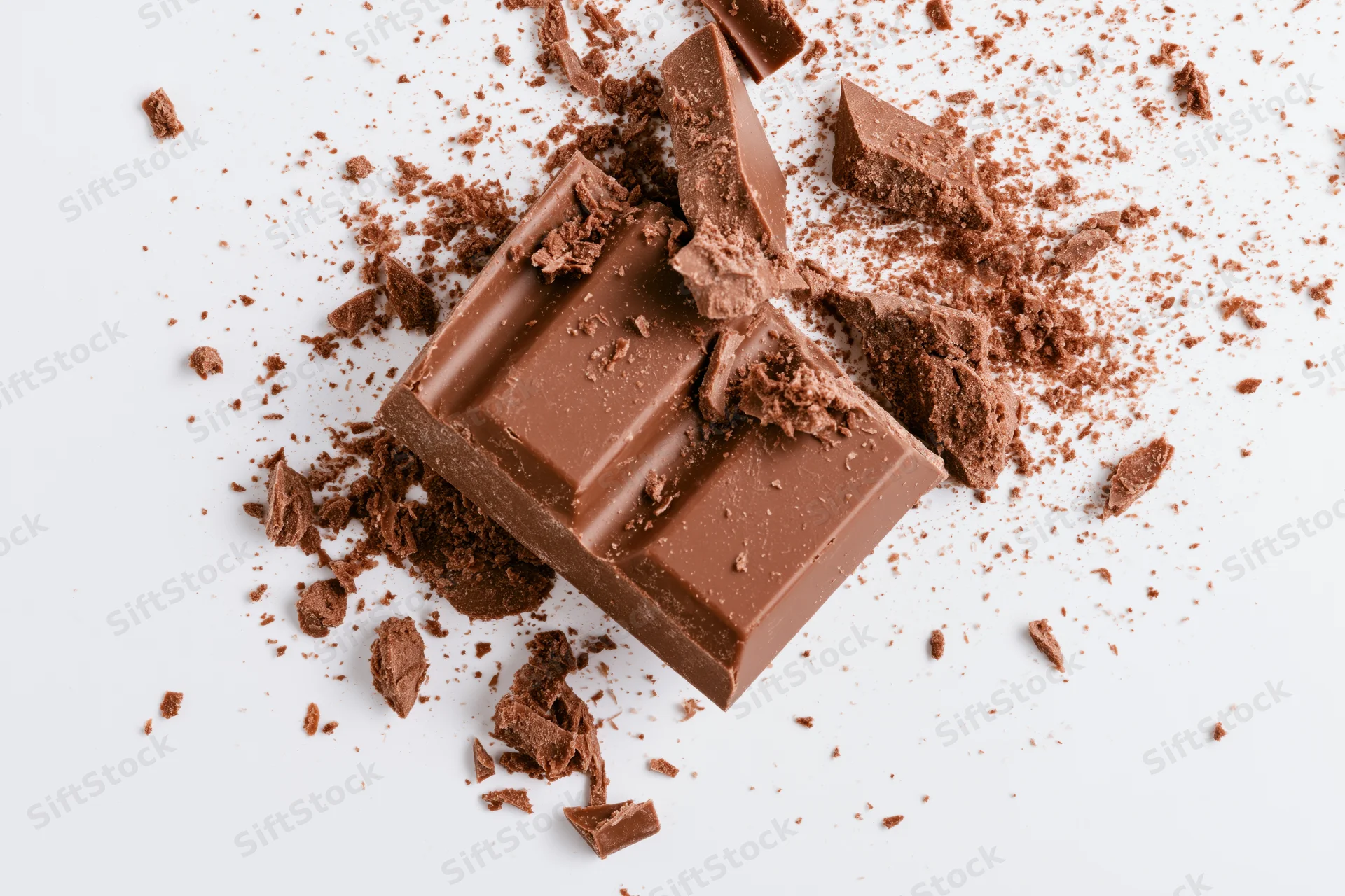 Broken milk chocolate bar pieces scattered on white background