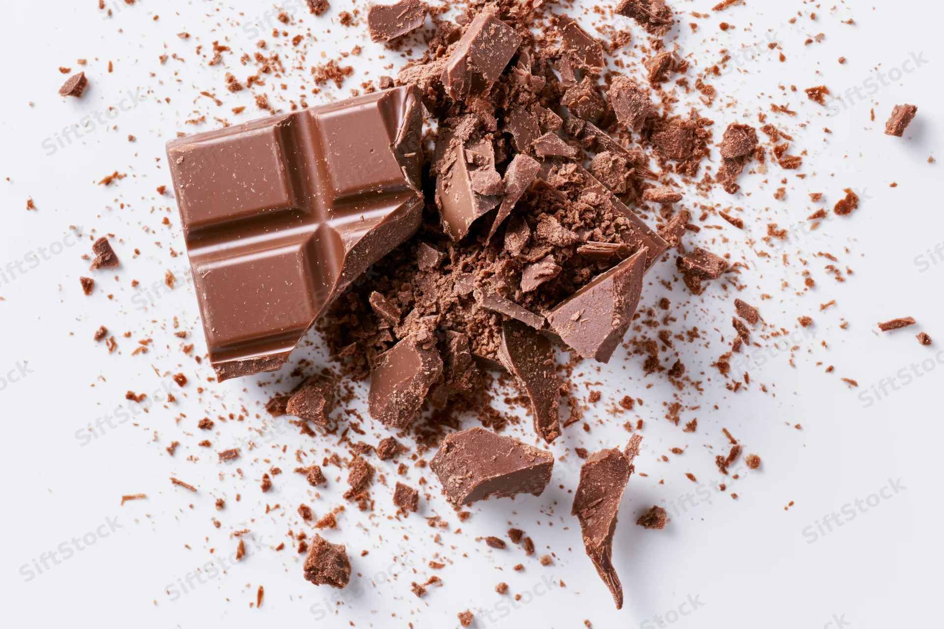 Broken milk chocolate bar pieces scattered on white surface