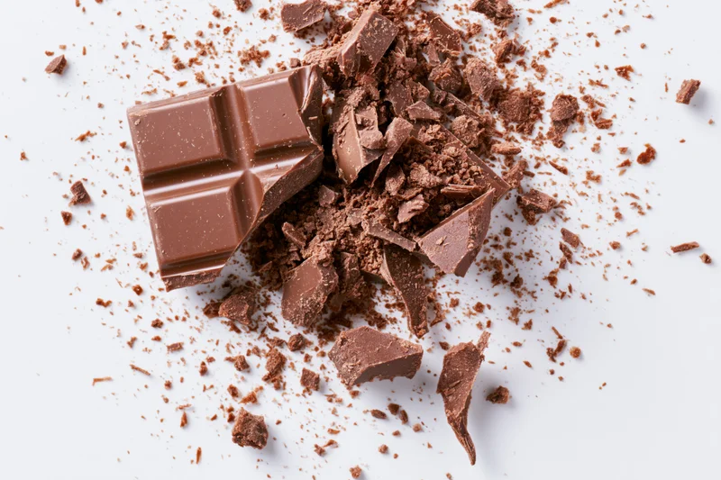 Broken milk chocolate bar pieces scattered on white surface