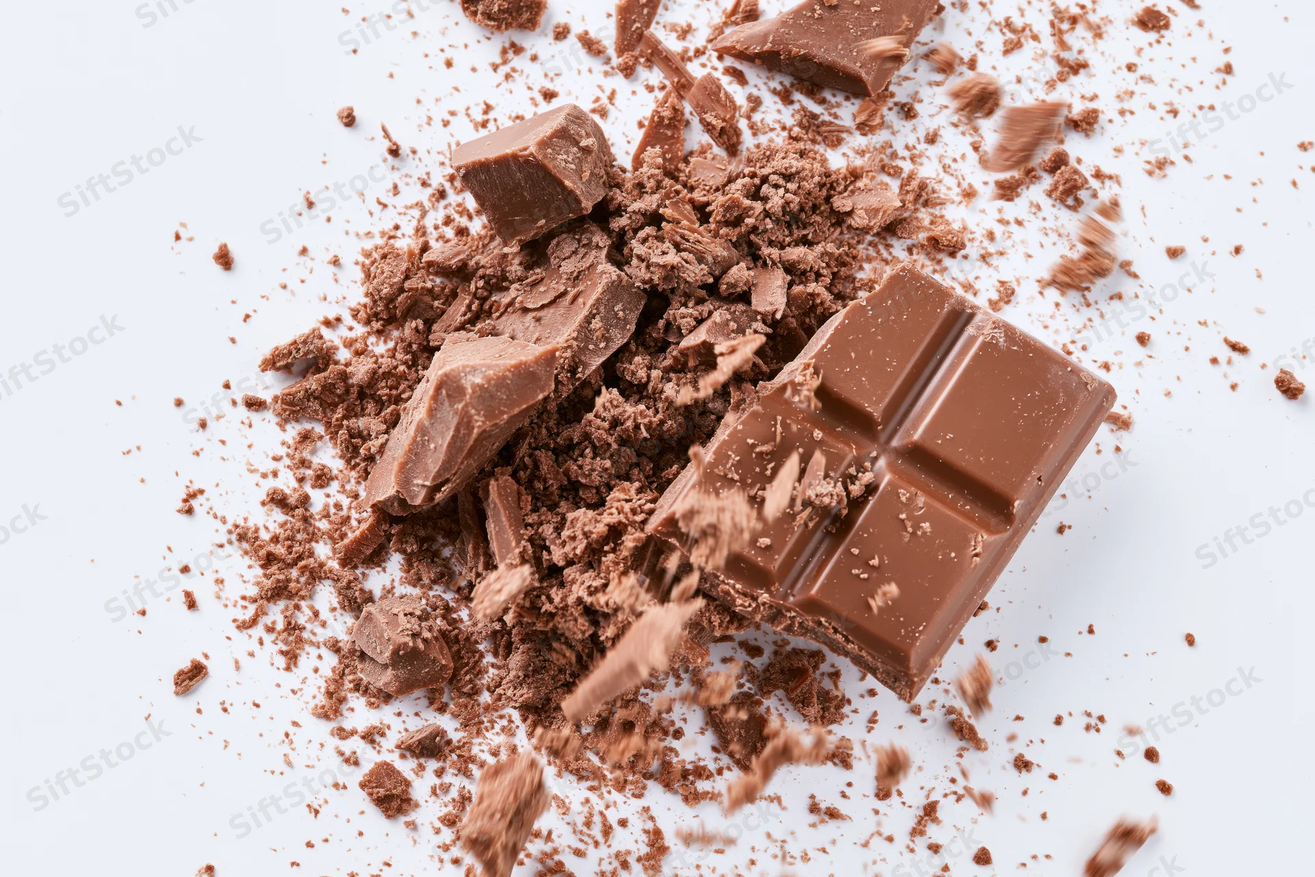 Broken milk chocolate bar pieces scattering midair on white background